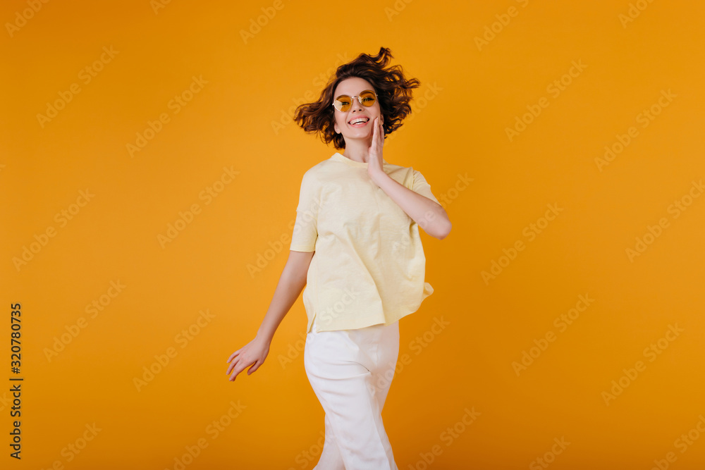 Pale girl with ecstatic face expression enjoying photoshoot in white summer attire. Pleased young woman in yellow t-shirt smiling while posing on orange background. Pale girl with ecstatic face expression enjoying photoshoot in white summer attire. Pleased young woman in yellow t-shirt smiling while posing on orange background.