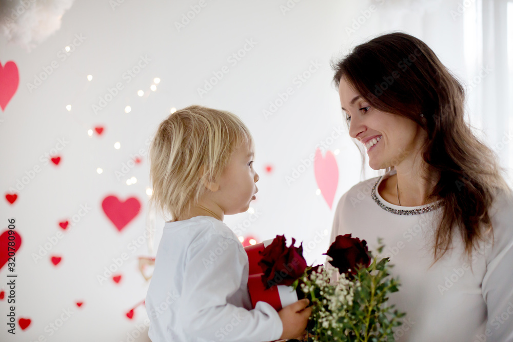 Cute blonde toddler boy, holding box in heart shape and flowers giving them to mom Cute blonde toddler boy, holding box in heart shape and flowers giving them to mom