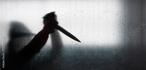 Obraz na plátně Shadow of hand holding big sharp knife behind frosted glass in the bathroom background