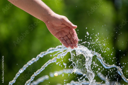Hand of a man in the spray of water of the fountain