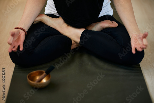 Close up of slim caucasian yogi woman sitting on the mat at home in lotus position and meditating. In front of her is Full Moon Singing Bowl.