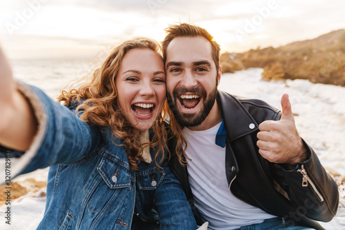 Image of caucasian couple taking selfie photo while walking by seaside