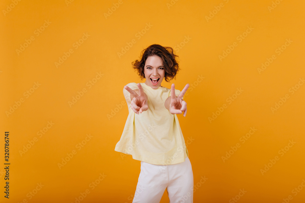 Gorgeous curly girl in yellow t-shirt funny dancing with sincere smile. Carefree brown-haired woman chilling in studio and laughing. Gorgeous curly girl in yellow t-shirt funny dancing with sincere smile. Carefree brown-haired woman chilling in studio and laughing.