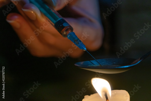 Dissolving drugs over a candle. needle and syringe pull the bubbling medicine out of the spoon. Hands of a drug addict with a syringe over a candle close-up