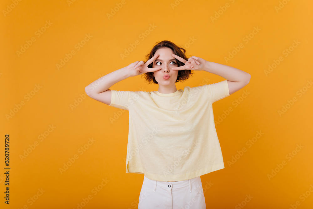 Lovable cute woman with tattoo posing with pleasure on yellow background. Indoor photo of stylish girl in white pants and oversize t-shirt. Lovable cute woman with tattoo posing with pleasure on yellow background. Indoor photo of stylish girl in white pants and oversize t-shirt.