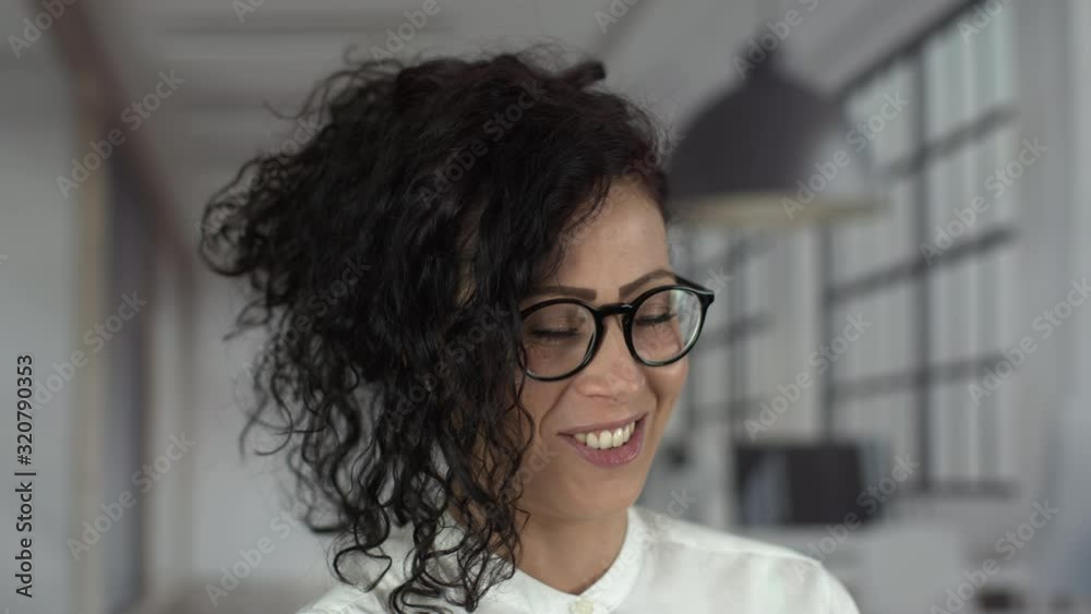 Portrait of happy young beautiful businesswoman with black glasses and curly hair laughing at the office. Successful woman at work looking at camera. Shot in 6k. Portrait of happy young beautiful businesswoman with black glasses and curly hair laughing at the office. Successful woman at work looking at camera. Shot in 6k.
