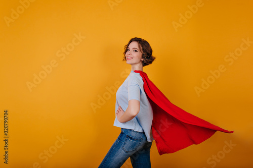 Fotografija Smiling supergirl in jeans standing in confident pose on yellow background