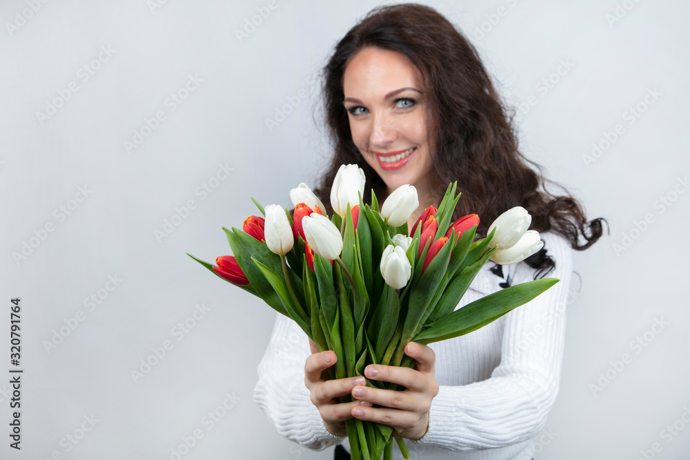 Concept, Valentine's Day greetings, Women's Day. Attractive woman holding a bouquet of tulips in her hands. Smile, joy, happiness, beauty.