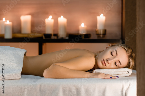 Spa concept. Young beautiful slim girl lies on massage table in anticipation of massage on a background of blurry burning candles.Front view, copy space