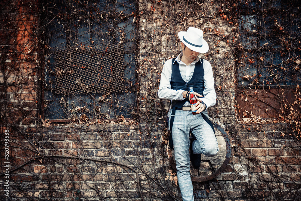 Fedora styled man with beer bottle against brick wall.