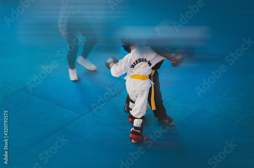 Martial Arts - Taekwondo.  Kids in traditional kimano, hard hats and gloves. Sports duel. For atmospheric, a motion blur film noise effect has been added. Text: Taekwondo is the name for martial art. © Uladzimir