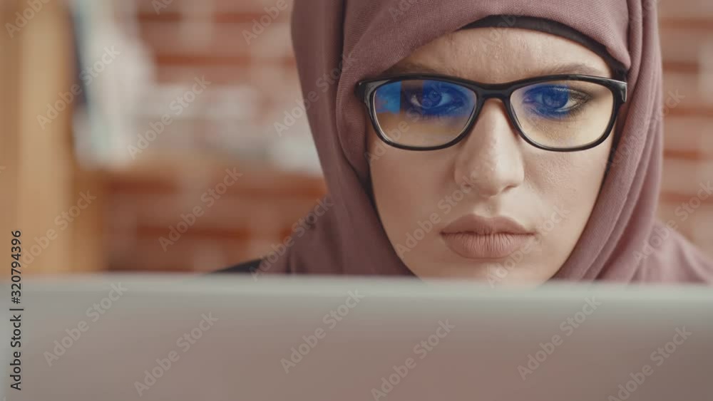 Close-up of the eyes of a Muslim woman working at a laptop, the view from the laptop cover. A view from the back of a laptop of a girl in a hijab Close-up of the eyes of a Muslim woman working at a laptop, the view from the laptop cover. A view from the back of a laptop of a girl in a hijab