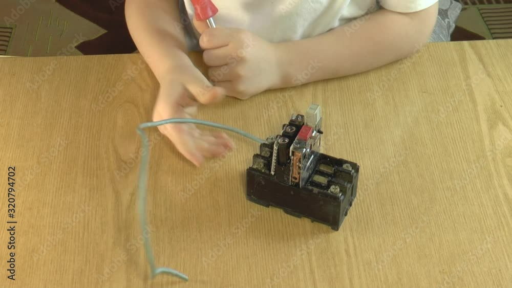 A kid sitting at a table tries to attach a wire to an electric relay ...