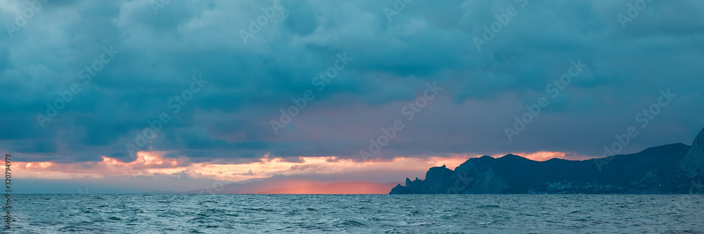 panoramic view of the sea coast with mountains and blue clouds, illuminated by the last rays of the sun