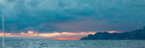 panoramic view of the sea coast with mountains and blue clouds  illuminated by the last rays of the sun