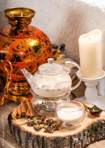 Traditional Indian tea in the teapot candle basking with milk and spices masala chai in a copper kettle and cup on wooden background in Russian restaurant. Food and drink, still life