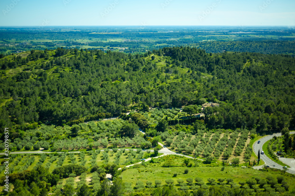 Scenic amazing view from Les Baux-de-Provence castle of Luberon valley in Provence, France. Sunny day and blue sky above green hills and vineyards. Cozy rural provencal landscape