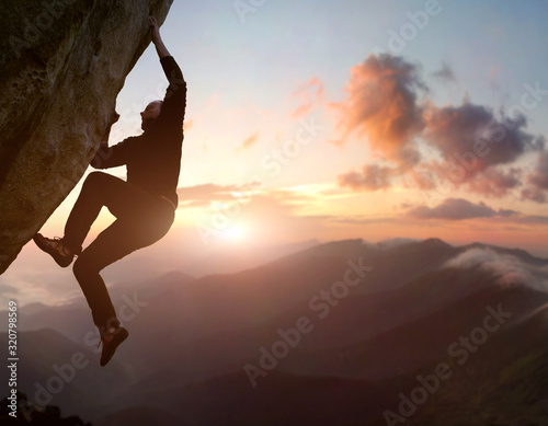 Rock climbing. Young male risky climber trying staying on challenging cliff route. Scenic mountain landscape with sunrise sky on background. Fail, difficulties, overcoming obstacles. Copy space