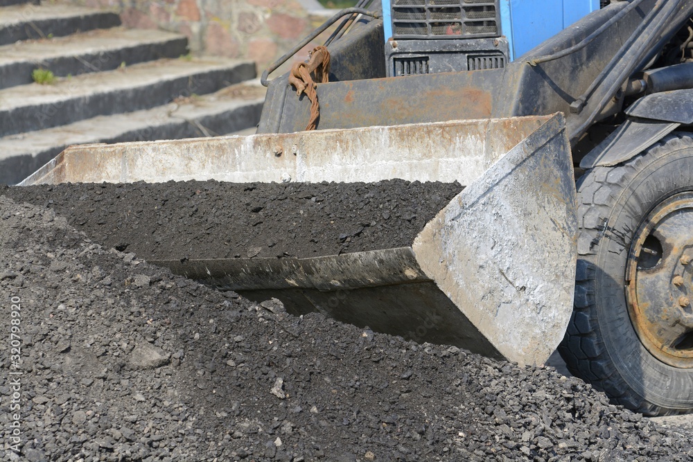 The mass of asphalt is accumulated in the excavator bucket for road repair