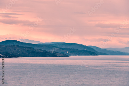 sea shore with mountain peaks in the clouds at a soft beige sunset