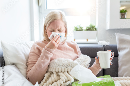 Cold And Flu. Portrait Of Ill Woman Caught Cold, Feeling Sick And Sneezing In Paper Wipe. Unhealthy Girl Covered In Blanket Wiping Nose. Healthcare Concept. Albino girl sick and drinking hot beverage
