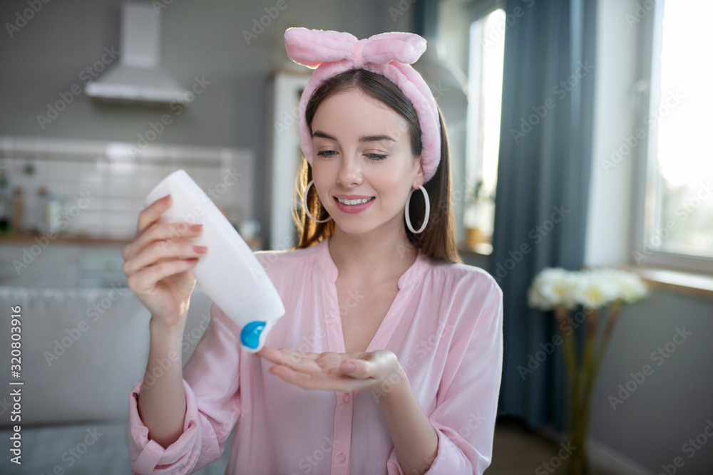Smiling pretty girl in a pink headband pouring lotion Smiling pretty girl in a pink headband pouring lotion