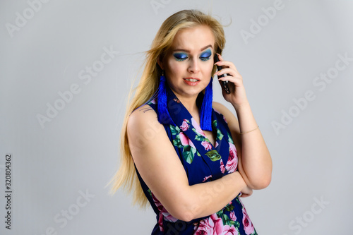 The model stands with the phone in her hands in various poses. Nice girl with fluttering hair and great make-up in front of the camera on a white background in a multi-colored dress.