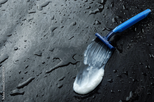 Blue sharp razor and smear of shaving cream on the wet dark surface.Empty space for text photo