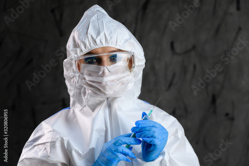 A doctor in a protective white suit with a syringe in his hands and blue rubber gloves stands in different poses on a gray background.