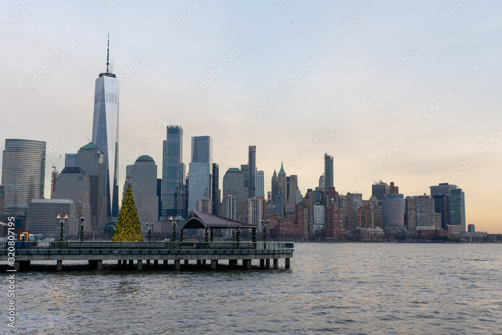 Fototapeta premium Skyline Dolnego Manhattanu w Nowym Jorku widziany z Jersey City z choinką podczas zachodu słońca