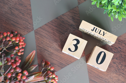 July 30. Date of December month. Number Cube with a flower leaves and bush on Diamond wood table for the background. photo