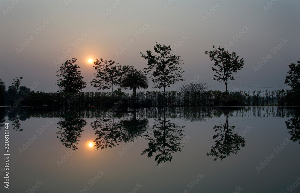 Tree line silhouette and its reflection from water surface in sunrise time Tree line silhouette and its reflection from water surface in sunrise time