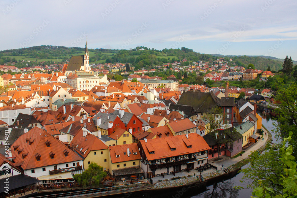 Vltava river flowing through the medieval village of Cesky Krumlov with a green hill at the background, in Czech Republic