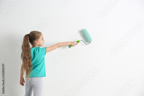 Little child painting with roller brush on white wall indoors
