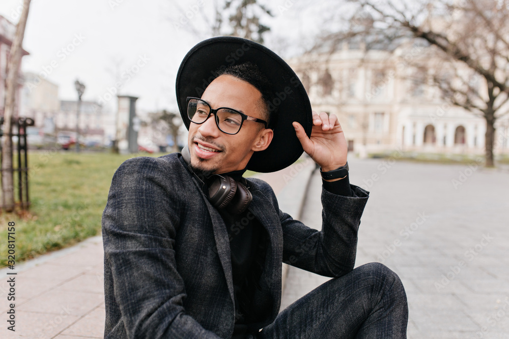 Young african man enjoying good spring day in park. Outdoor photo of amazing male model sitting in square and waiting someone. Young african man enjoying good spring day in park. Outdoor photo of amazing male model sitting in square and waiting someone.
