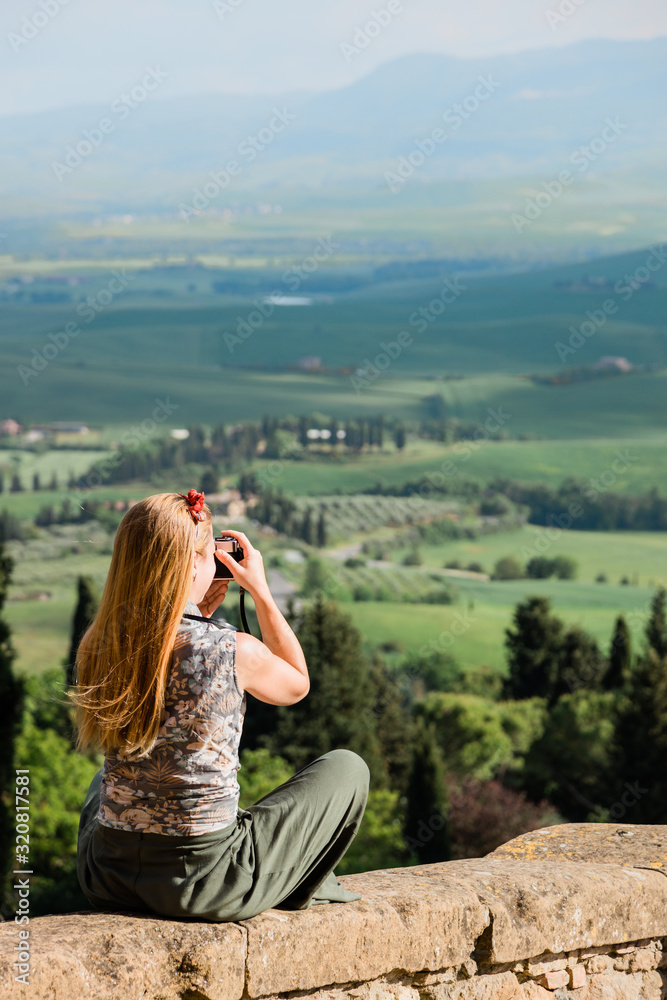 Young female traveler taking a photo of a beautiful landscape in Tuscany, Italy