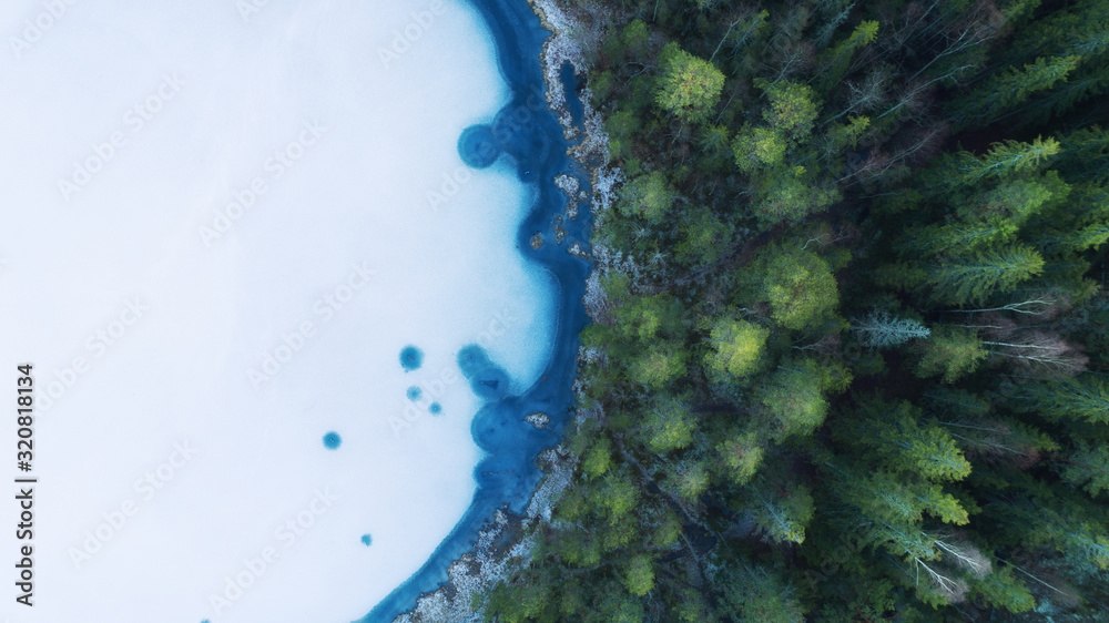 Aerial view of a beautiful frozen lake and forests in winter. Photo of the northern nature of Finland with a drone.