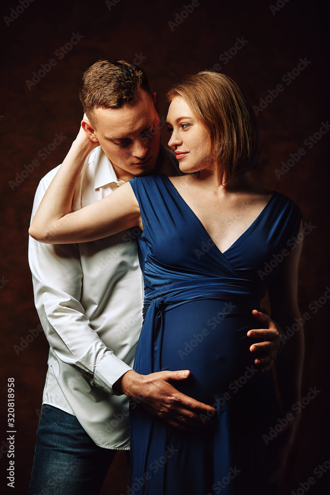 Fototapeta premium Pregnant couple posing for the camera on a brown background, low key. Fashion Pregnancy Concept. Copy space, brown background.