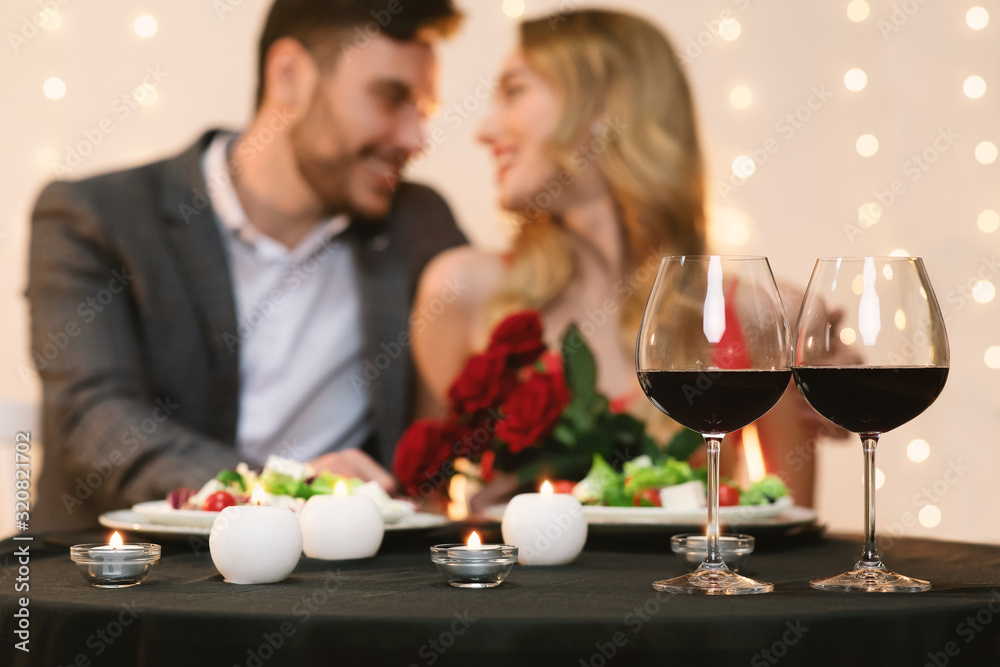 Affectionate couple dating in restaurant, glasses with red wine in foreground Affectionate couple dating in restaurant, glasses with red wine in foreground