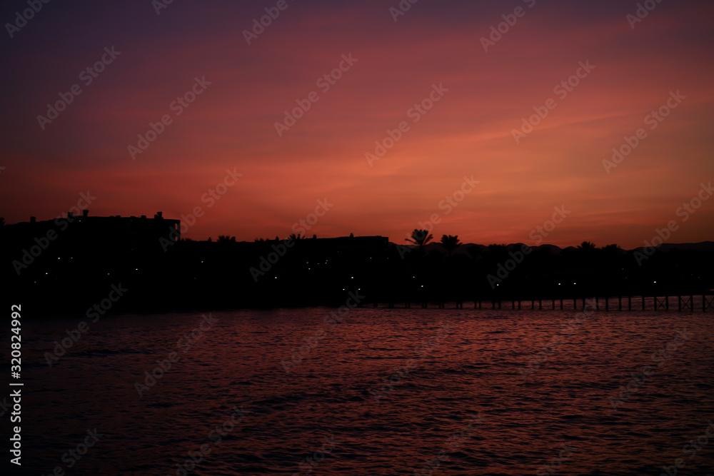 Purple sunset against the background of the silhouette of a pontoon bridge, hotel and palm trees at dusk