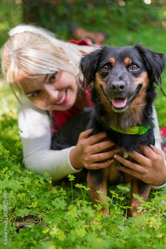 Happy and smiling blonde girl next to her black dog among the clovers and green nature.
