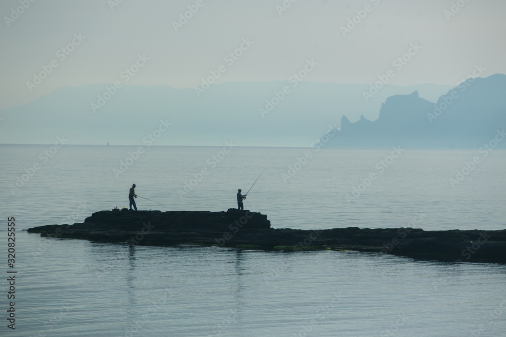 Fishermen with fishing rods catch fish on a cape near the sea