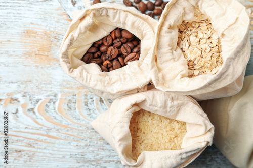 Cotton eco bags with cereals and coffee beans on wooden table, flat lay