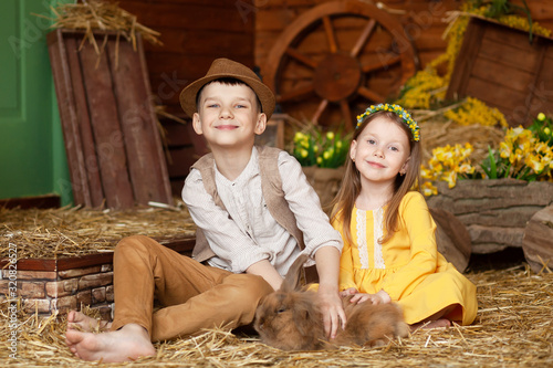 Easter! Cute little happy children, a boy and a girl in the hay with animals - chickens and a rabbit on Easter day. Children are having fun, playing and hugging.