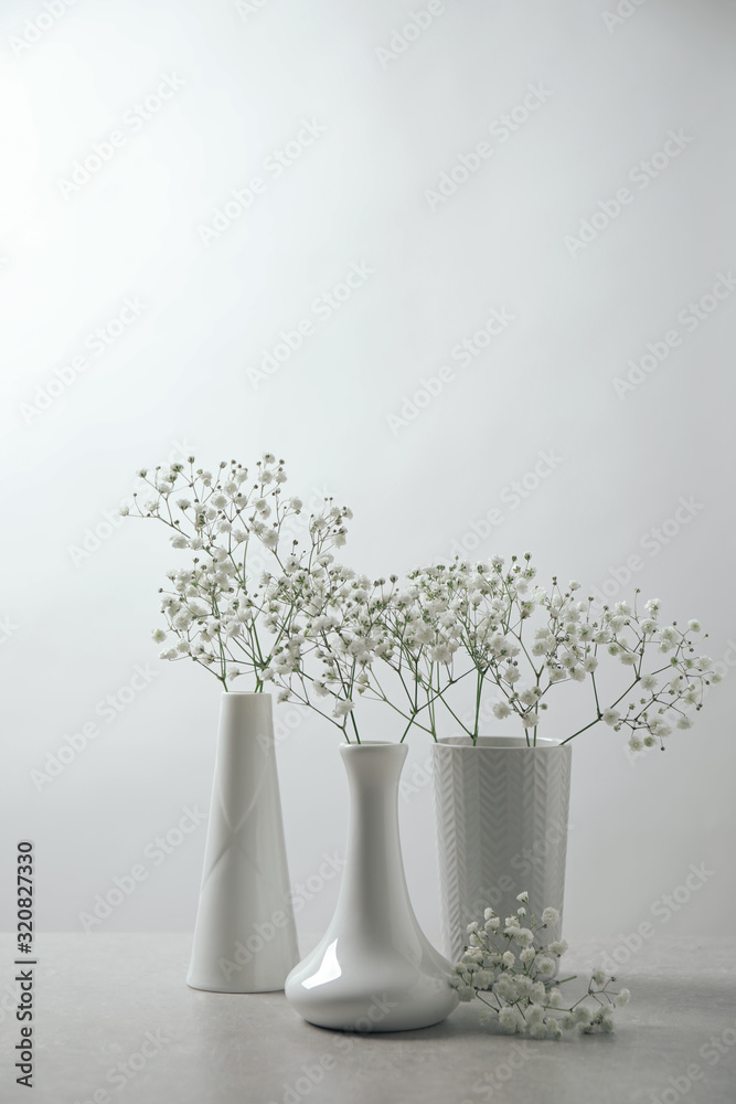 Gypsophila flowers in vases on table against white background