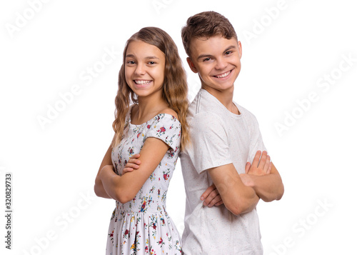 Portrait of smiling teen boy and girl standing back to back. Teenagers look at camera. Happy children in casual clothes with folded arms, isolated on white background. Friendship and love concept.