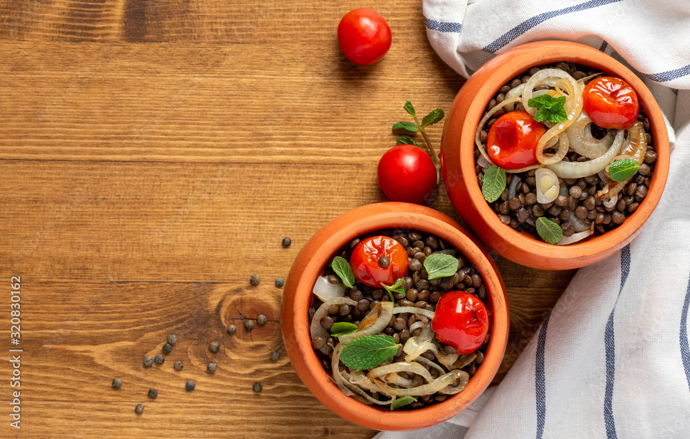 Cooked green lentils with tomatoes, onions and mint in pots on a wooden background, top view, copy space. Vegan and vegetarian food, Mediterranean cuisine.
