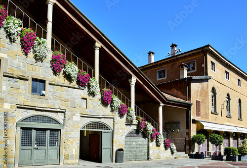 Bergamo, Italy - Campanone, town hall with stairs and columns, decorated with red and white flowers, buildings in the summer afternoon.