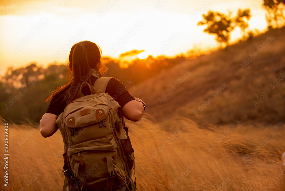 Traveler asian woman with backpack walking in gold meadow enjoying sunset on peak mountain at natural park Traveler asian woman with backpack walking in gold meadow enjoying sunset on peak mountain at natural park