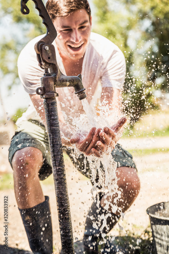 Young man spalshes himself with water on a farm. Laurel, Montana, USA photo